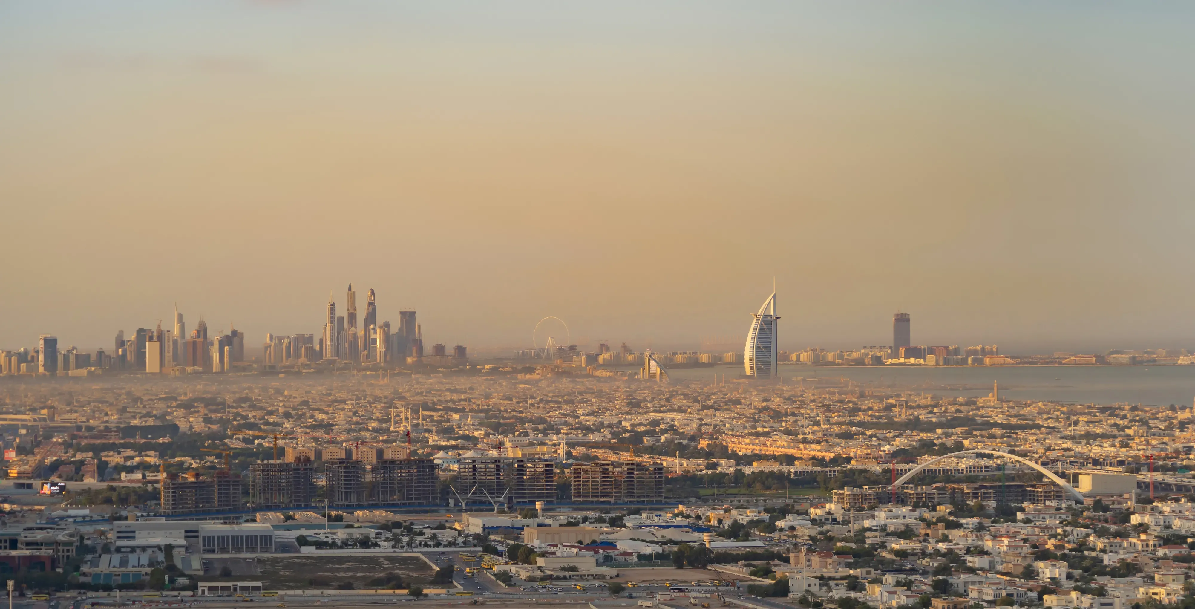 Aerial perspective of Dubai at dusk, displaying the city’s extensive skyline with Burj Al Arab and other notable skyscrapers, spread across the urban landscape and coastline.